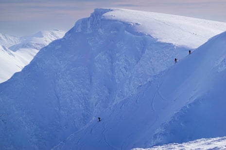 Three people ski down the slope of a vast mountain covered in snow