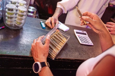 A shop owner takes a cannabis cigarette from a container of them to show a customer