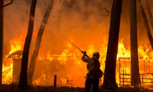 A CalFire firefighter attempts to cool down the side of a home in Magalia, California, near Paradise as the wildfire continues to burn out of control.