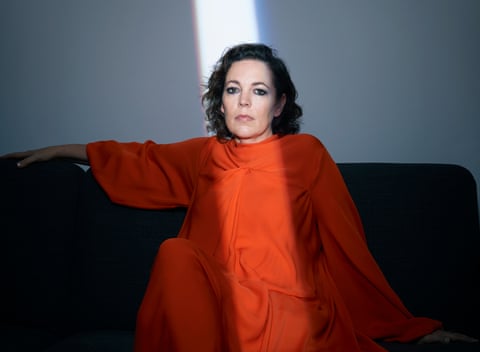 Olivia Colman in orange dress on brown sofa, with shaft of light coming down across her face, October 2021