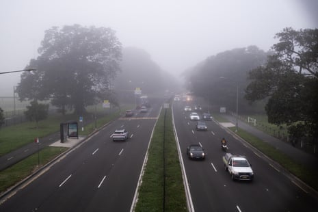 Cars drive on a roadway beneath heavy fog.
