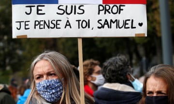 Woman wearing facemask in crowd with placard saying: I am a teacher I think of you, Samuel