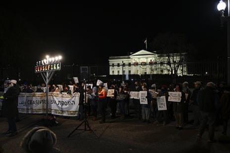 People attend the event carrying signs and standing behind a menorah candle, with the White House in the background