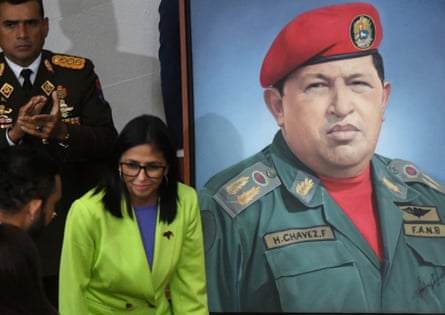 a woman in a green suit stands next to a painting of a man in military fatigues and a red beret