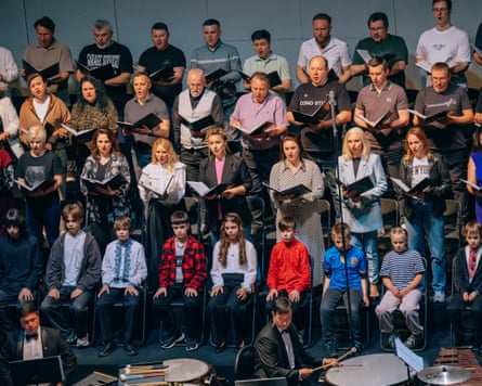 Children sit in a row with adult choir members standing behind them