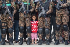 A girl in red stands between fighters in camouflage clothing holding guns