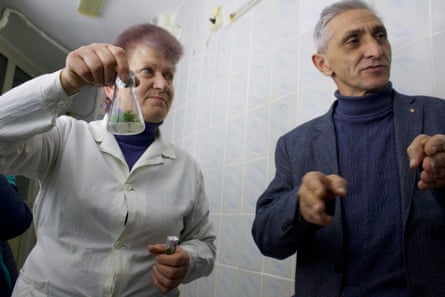 Larisa Kolder, dressed in a white lab coat, holds up a conical flask containing a Moehringia hypanica specimen, next to Volodymyr Hrabovyi, who is gesturing as he speaks
