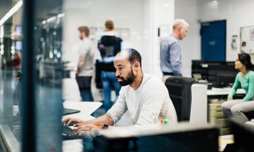 Man in office typing surrounded by other workers.