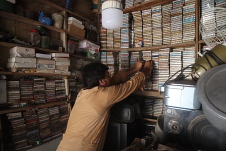 Man in a tiny shop crowded with cassette players and music cassettes on shelves lining the walls. 