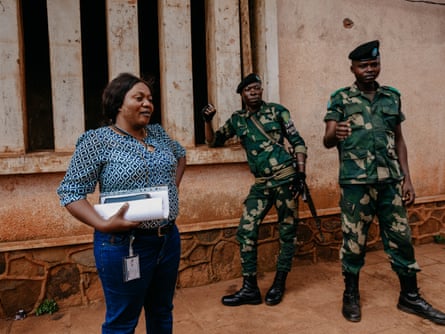 A woman holds papers as two men in uniform stand about