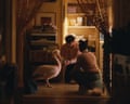 Two people kneel on a kitchen floor beside a white pelican, viewed through a doorway at night.