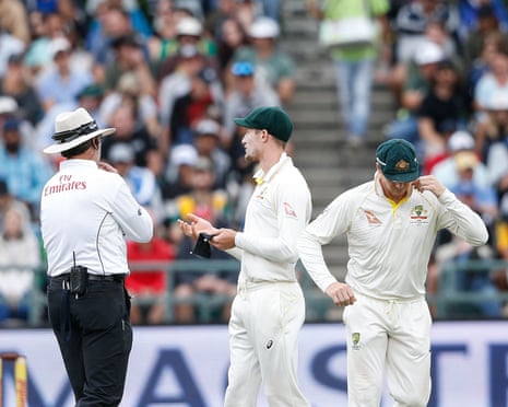 Cameron Bancroft talks to an umpire on the field as Steve Smith looks at the ground