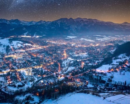 Looking down on the lights of a town in winter, from surrounding mountains. Snow lies on the ground
