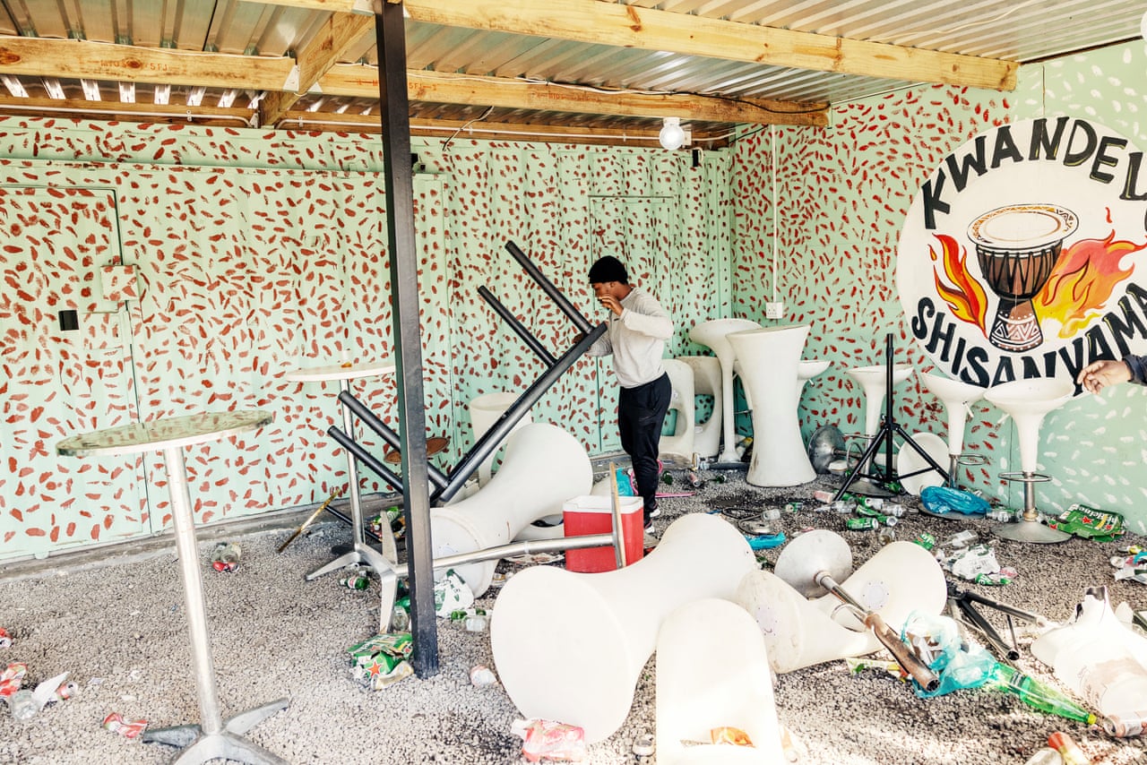 A man picks up an upturned table amid scattered chairs and debris