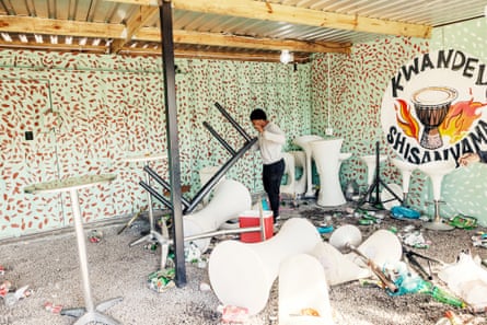 A man picks up an upturned table amid scattered chairs and debris