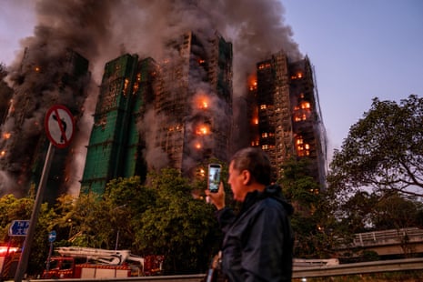 A man uses his phone to record the smoke and flames engulfing the complex.