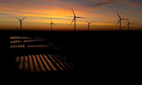 Wind turbines operate as the sun rises at a solar energy park near Klettwitz, Germany: the solar arrays shine in the darkness while the wind turbines are silhouetted against the orange sky
