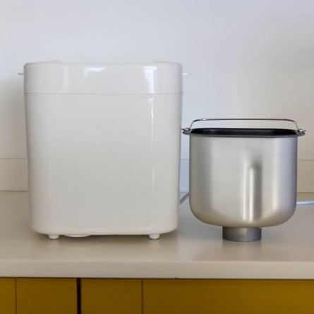 A white Russell Hobbs bread maker stands beside its removable metal baking pan on a counter