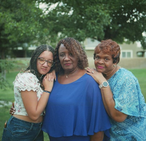 Three women stand in the back yard of a home surrounded by trees.