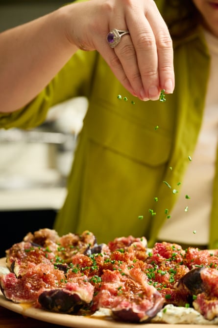Hands sprinkling finely chopped chives over a platter of figs and labneh.
