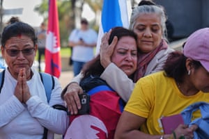 One woman prays while another, held by a third woman, weeps
