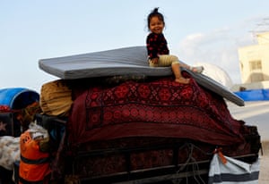 A smiling girl sits on top of mattresses and other belongings