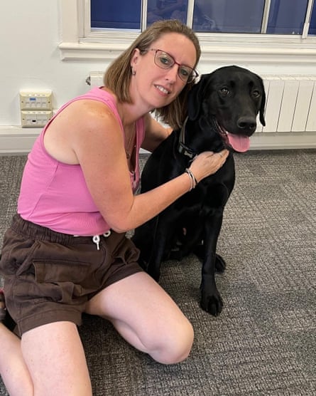 Sarah sitting on the floor with her arms around a black lab
