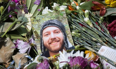 A portrait of a young man lies atop bouquets of flowers at a memorial
