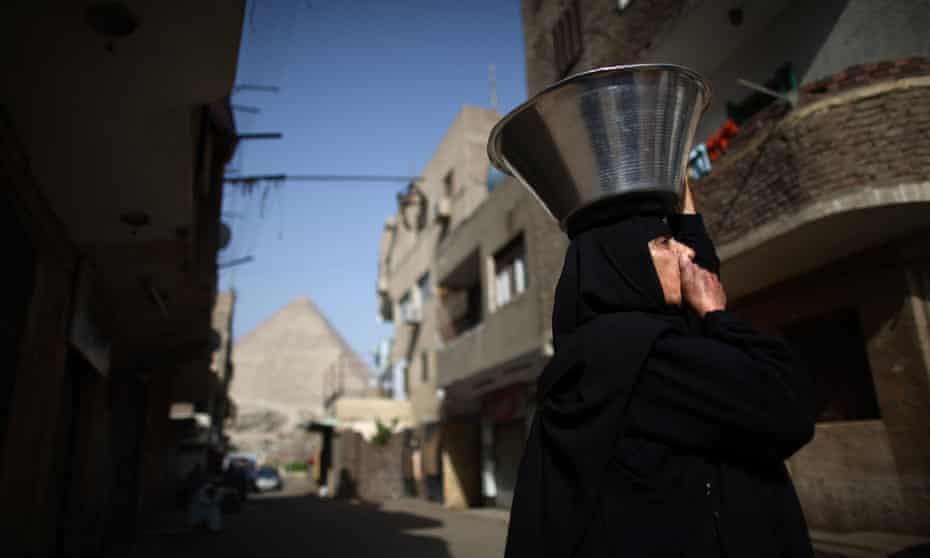 A woman carries a food bowl on her head in the village of El Saman in sight of the Great Pyramid of Cheops in Giza, Egypt.