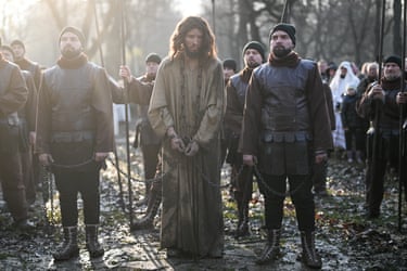 Image 27: An actor dressed as Jesus in a muddied costume and chains surrounded by actors dressed as soldiers