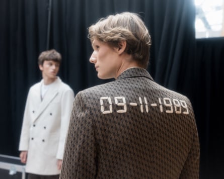 A male model with “09-11-1989” on the shoulders of his blazer, and another model in a coat in the distance