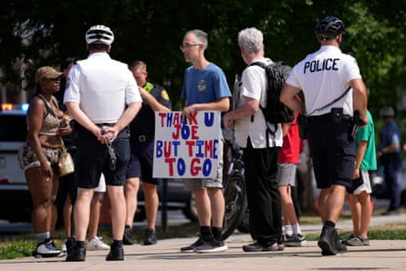 people stand around man wearing blue shirt and holding a red, white and blue sign reading ‘Thank U Joe But Time To Go.’