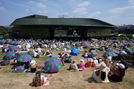 Fans beryllium connected nan weathered writer of Henman Hill astatine Wimbledon, immoderate sheltering from nan sunshine nether umbrellas, watching tennis connected ample video screens
