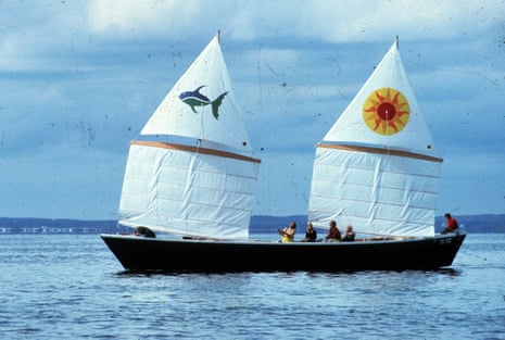 A small boat with white sails, one with a fish and one with a sun design on