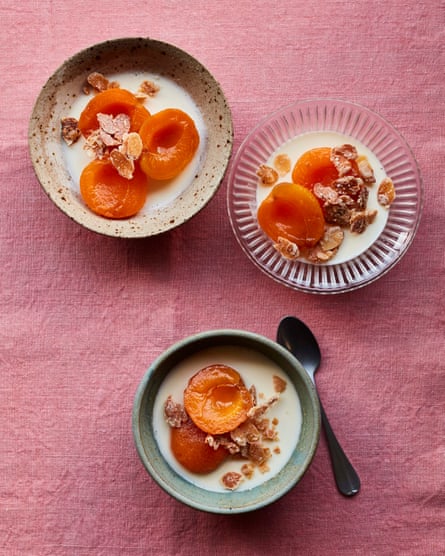 Three bowls of poached apricot halves with almond cream on a pink tablecloth.
