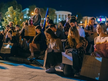 People kneel on one knee at night in a square with placards