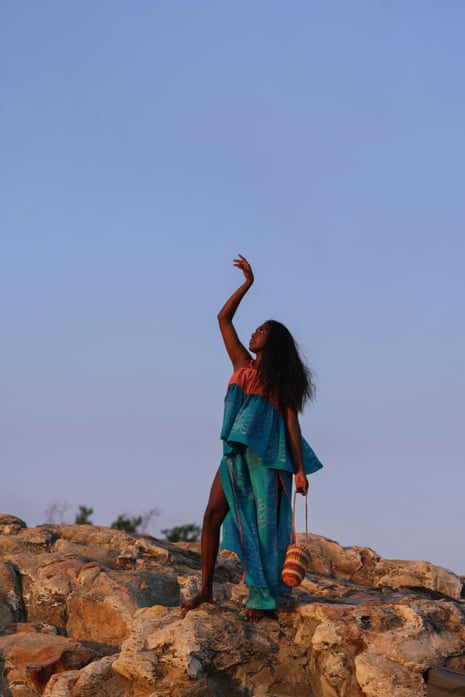 A woman in a teal outfit strikes a pose with one arm in the air