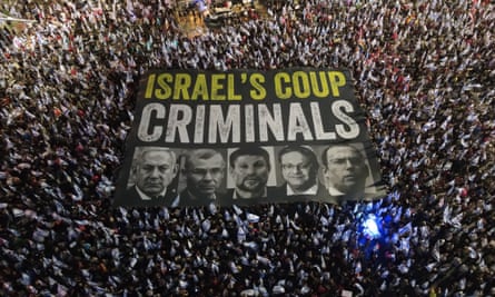 huge crowd holding up banner that says ‘israel’s coup criminals’ with images including netanyahu