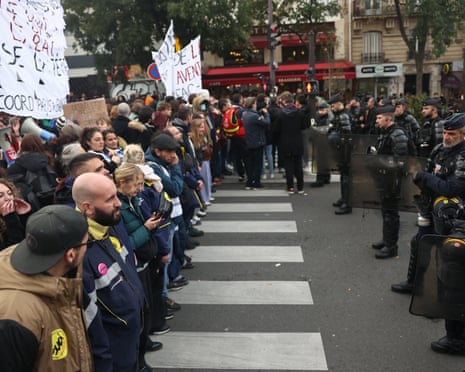 Riot police with shields face a line of protesters holding banners during a Paris protest