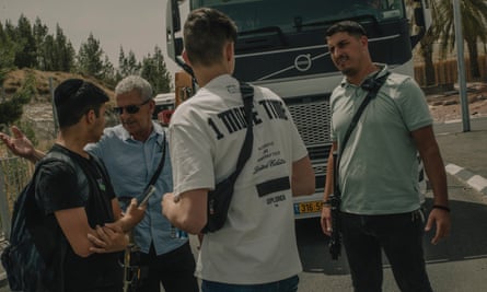 Four people stand in front of a lorry. One is carrying a gun.