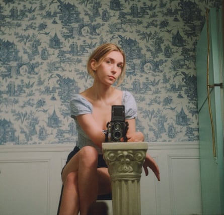woman with camera sits on chair in front of wallpapered wall