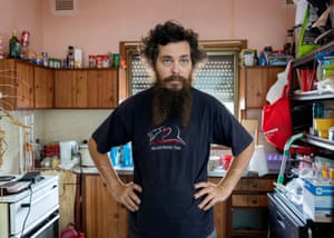 A man poses in the middle of a cluttered kitchen.