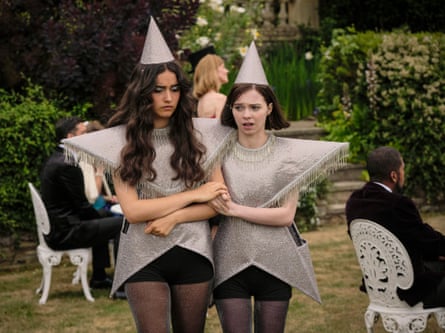 Two girls in star costumes with pointed hats walk through a garden arm in arm