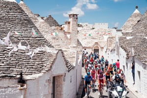 Pack of cyclists moving through narrow street of old buildings.