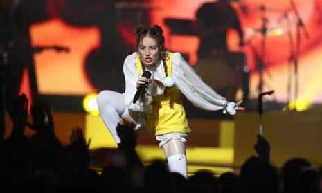 Australian singer Jaguar Jonze, who in 2021 made allegations of sexual assault in the music industry. She is on stage wearing a white shirt and short yellow overalls, singing into a microphone