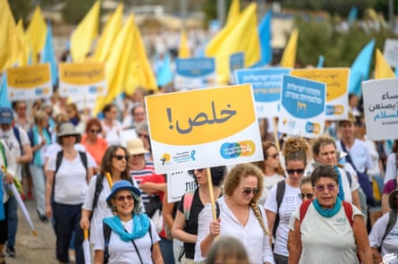 A large number of women march holding signs and blue and yellow flags.