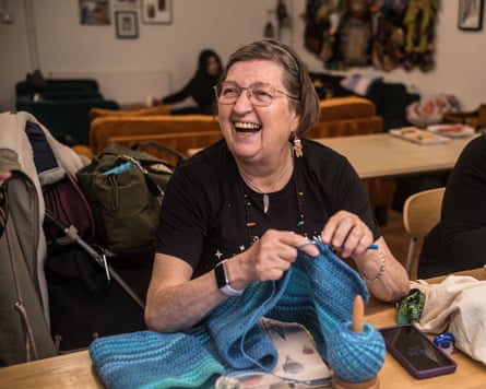 Dot McEvoy smiles as she sits at a table knitting