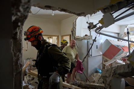 Two rescuers walk Haim Rasin through a damaged flat