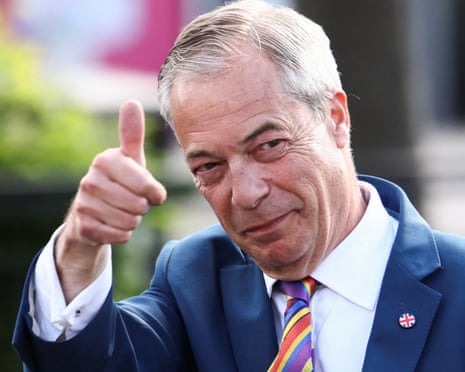 Nigel Farage in a blue suit and striped tie gives a thumbs up gesture outdoors
