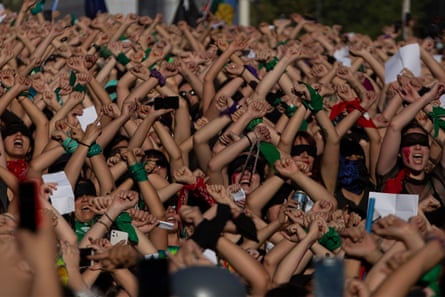 A large crowd of women, many wearing green, with their arms above their heads and their wrists crossed